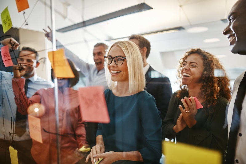 Smiling young businesswoman and her diverse team brainstorming ideas with sticky notes on a glass wall while working together in a modern office